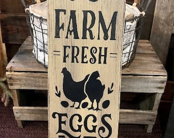 May include: A rustic wooden sign with black lettering that reads "FARM =FRESH= EGGS • PURE • ORGANIC • Laid daily". The sign features a silhouette of two chickens and eggs.