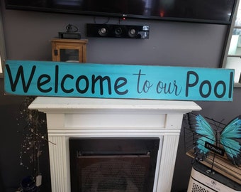 May include: A turquoise blue wooden sign with black lettering that reads "Welcome to our Pool".