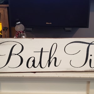 May include: White wooden sign with black script lettering that reads "Bath Time".