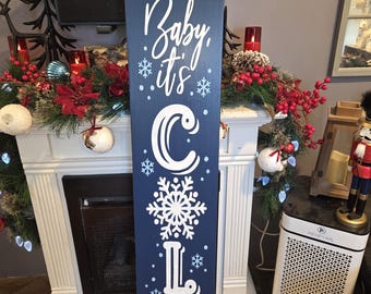 Può includere: Un cartello in legno blu navy con scritte bianche che recita "Baby, it's cold outside". Il cartello presenta un disegno a fiocco di neve ed è decorato con piccoli fiocchi di neve. Il cartello è un oggetto di arredamento per la casa a tema invernale.