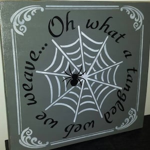 May include: A grey wooden sign with white and black lettering. The sign reads "Oh what a tangled web you weave..." with a white spider's web and a black spider in the centre.