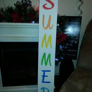 May include: A white wooden sign with the word "SUMMER" spelled out in rainbow colors. Each letter is a different color, starting with red and ending with blue.