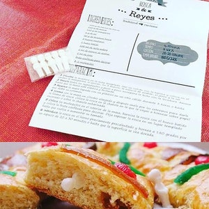 Puede incluir: Primer plano de una rosca de reyes cortada, un pastel tradicional español, con una figurita blanca en su interior. La rosca está decorada con caramelos verdes y rojos. La rosca está horneada a un color dorado.