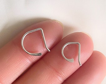 May include: Two silver-colored, minimalist earrings. Each earring has a curved bottom and a straight top, forming a D-shape. The earrings are displayed on a light-colored background.