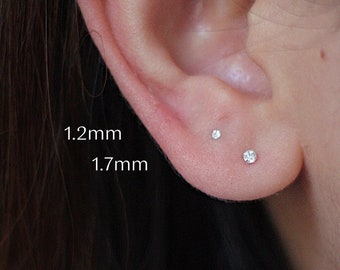 Puede incluir: Primer plano de la oreja de una persona con dos pequeños pendientes de diamantes. Los pendientes miden 1,2 mm y 1,7 mm.