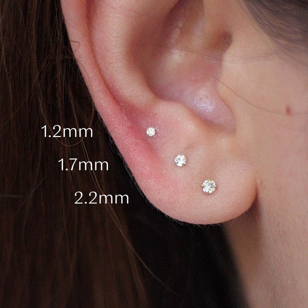 Könnte beinhalten: Drei verschiedene Größen von Ohrsteckern, 1,2 mm, 1,7 mm und 2,2 mm, sind in einem Ohr einer Person zu sehen. Die Ohrringe sind klein und zart und aus Silber gefertigt.