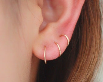 May include: Close-up of a person's ear with four gold hoop earrings. The earrings are stacked on top of each other, with the smallest earring at the top and the largest earring at the bottom.