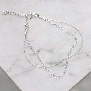 May include: A silver chain bracelet with two different chain styles. The bracelet has a lobster clasp closure.