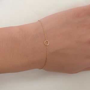 Peut inclure: Bracelet en or fin avec un petit pendentif en forme de cercle ouvert. La chaîne est délicate. Le bijou est présenté sur un fond clair. Le pendentif est un cercle simple et ouvert.