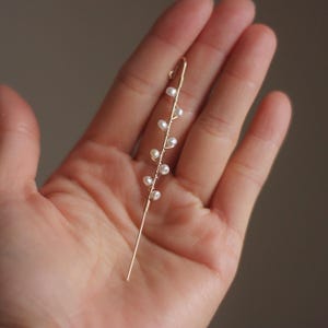 Puede incluir: Un delicado pendiente de oreja dorado con un dise&ntilde;o lineal con peque&ntilde;as perlas blancas. El pendiente tiene un poste largo y recto y una parte superior curvada para asegurar a la oreja. Las perlas est&aacute;n espaciadas uniformemente a lo largo del alambre.