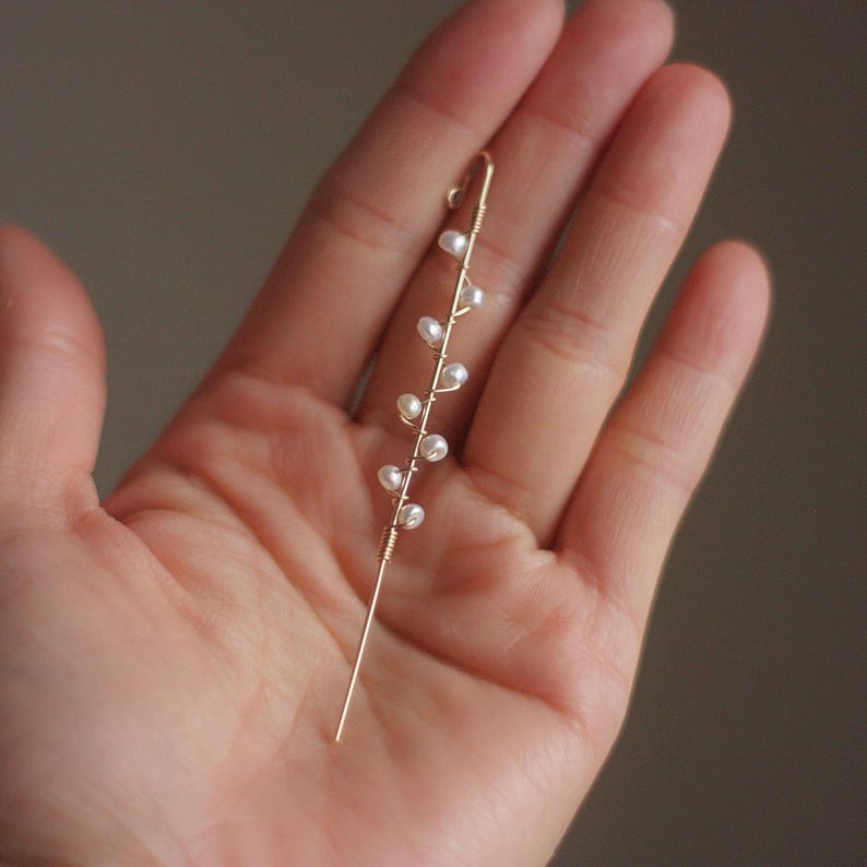 Puede incluir: Un delicado pendiente de oreja dorado con un dise&ntilde;o lineal con peque&ntilde;as perlas blancas. El pendiente tiene un poste largo y recto y una parte superior curvada para asegurar a la oreja. Las perlas est&aacute;n espaciadas uniformemente a lo largo del alambre.