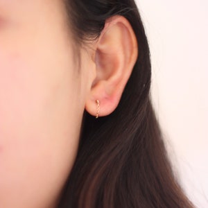 May include: A close-up of a gold chain earring. The earring features a small stud at the earlobe and a delicate chain that hangs down. The earring is a simple, elegant design.