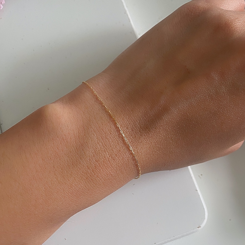 May include: A delicate gold chain bracelet on a person's wrist.