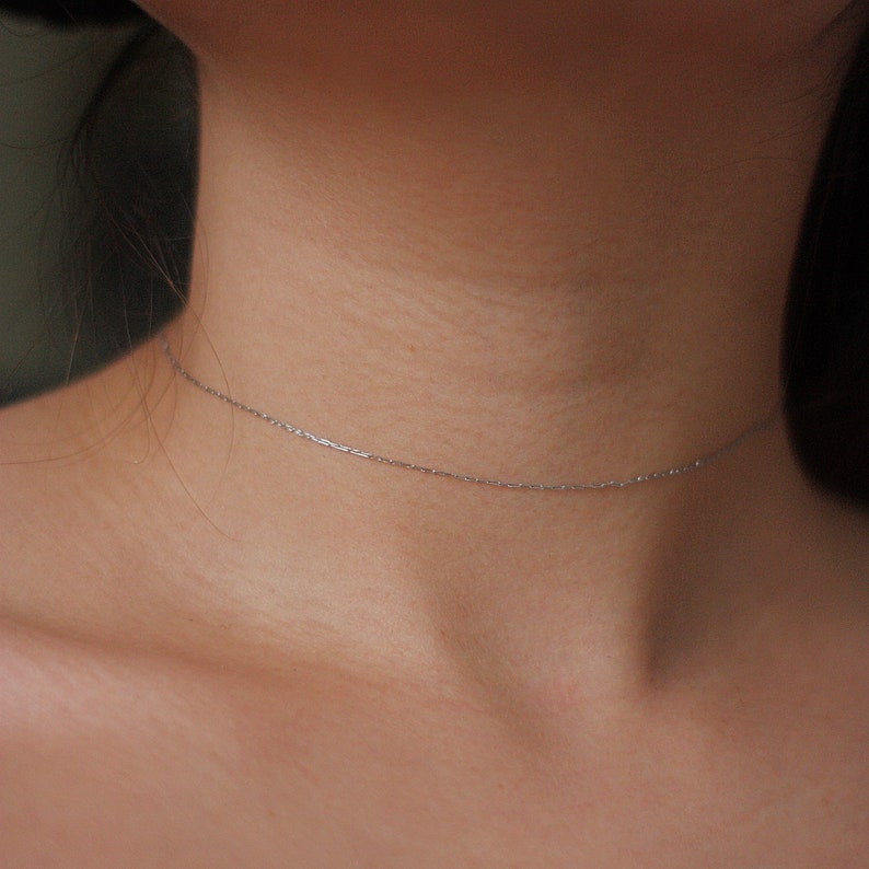 May include: A delicate silver chain necklace worn around the neck of a person.