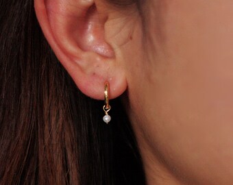 May include: Gold hoop earrings with a small pearl dangling from each hoop.