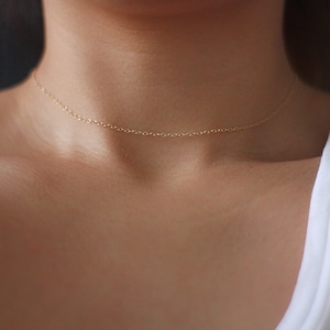 May include: A delicate gold chain necklace, worn as a choker, on a person's neck.