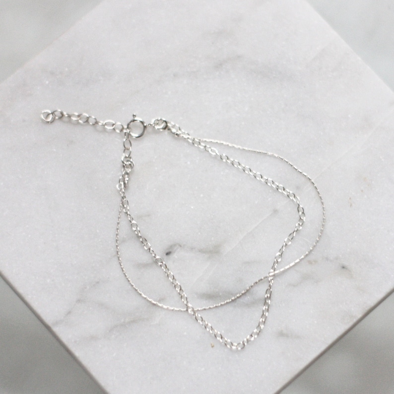 May include: A silver chain bracelet with two different chain styles. The bracelet has a lobster clasp closure.