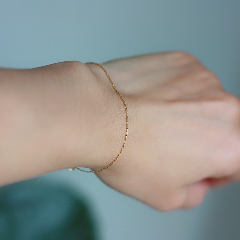 May include: A delicate gold chain bracelet on a person's wrist.