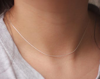May include: A delicate silver chain necklace on a person's neck. The chain is thin and has a subtle shine.