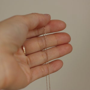 May include: A close-up of a hand holding a delicate gold chain necklace.