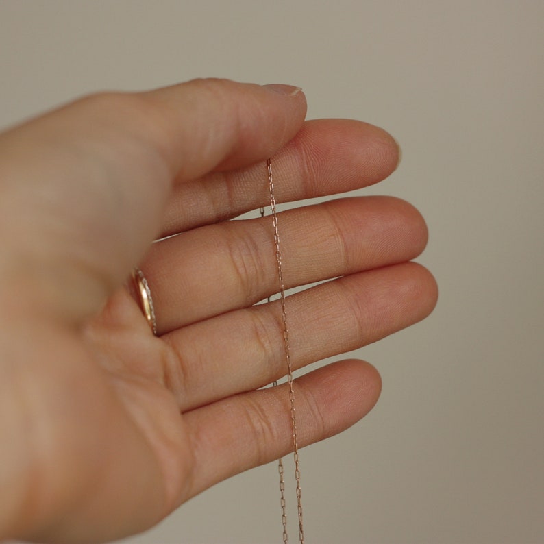May include: A close-up of a hand holding a delicate gold chain necklace.