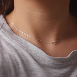 May include: A delicate silver chain necklace with a small circle pendant.