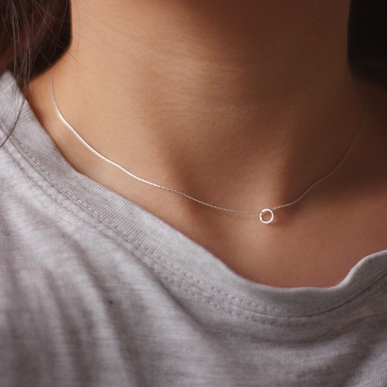May include: A delicate silver chain necklace with a small circle pendant.