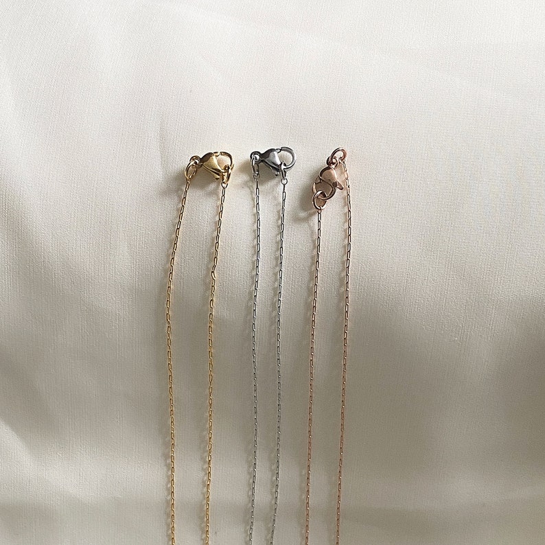 May include: Four silver chains with lobster clasps. The chains are different lengths and are hanging against a white background.