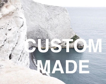 May include: A white text overlay on a scenic image of a white cliff overlooking a blue body of water. The text reads "CUSTOM MADE".