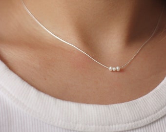 May include: A delicate silver chain necklace with three small white pearls.