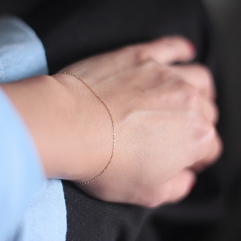 May include: A delicate gold chain bracelet on a person's wrist.