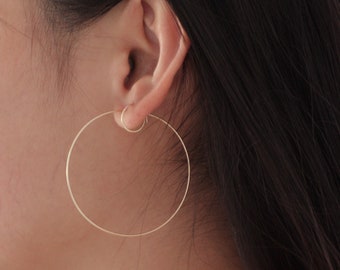 May include: A pair of gold hoop earrings. The earrings are large and circular, and they are worn in the wearer's ear.