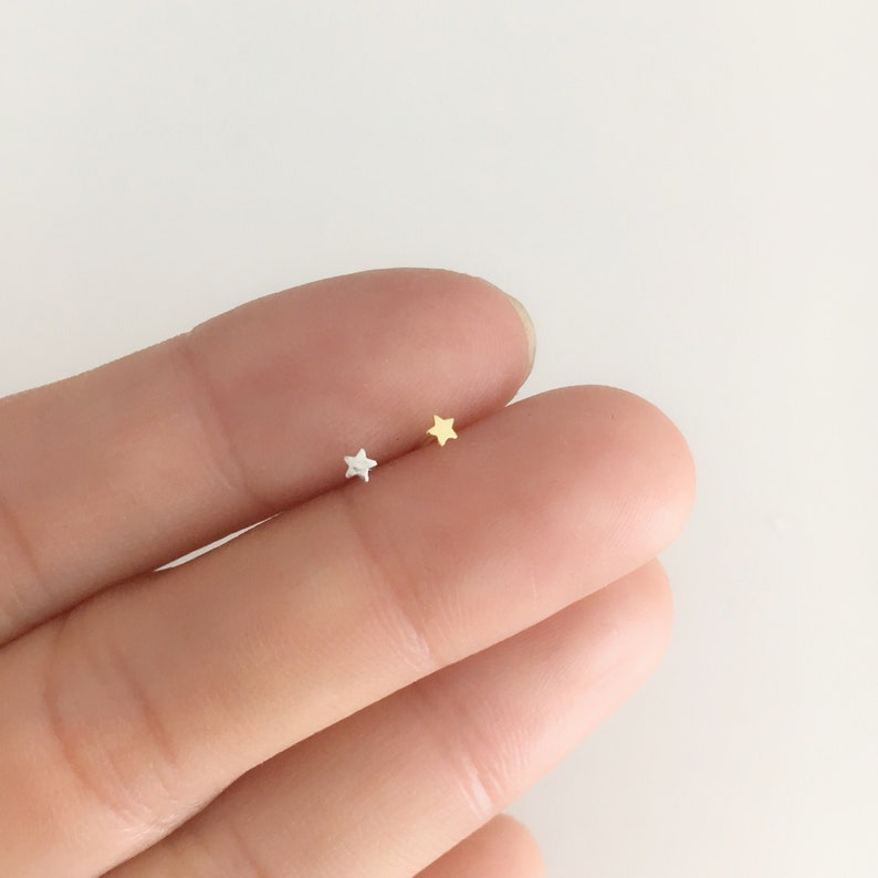 Puede incluir: Se muestran dos peque&ntilde;os pendientes en forma de estrella, uno plateado y otro dorado. Los pendientes tienen un dise&ntilde;o minimalista. Probablemente est&aacute;n hechos de metal y son adecuados para el uso diario.
