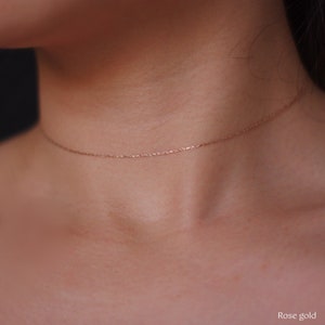May include: Rose gold necklace. A delicate, thin chain necklace in rose gold color is displayed. The necklace is worn around the neck. The image is a close-up shot, highlighting the necklace's fine details. The text "Rose gold" is in the bottom right corner.