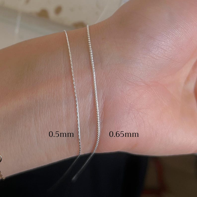May include: Two silver chains on a person's wrist, one is 0.5mm thick and the other is 0.65mm thick.