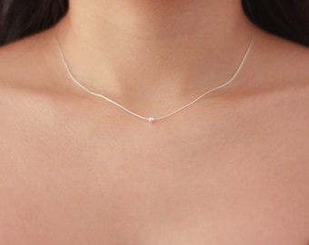 May include: A delicate silver chain necklace with a small, round pendant.