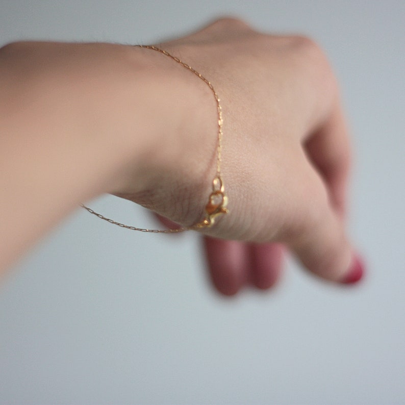 May include: A gold chain bracelet with a small, delicate charm on a person's wrist.