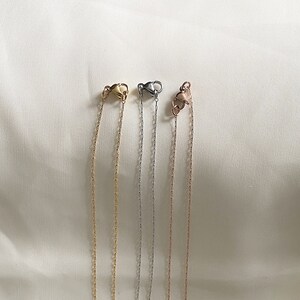 May include: Four different chain necklaces with lobster claw clasps. The chains are gold, silver, and rose gold.