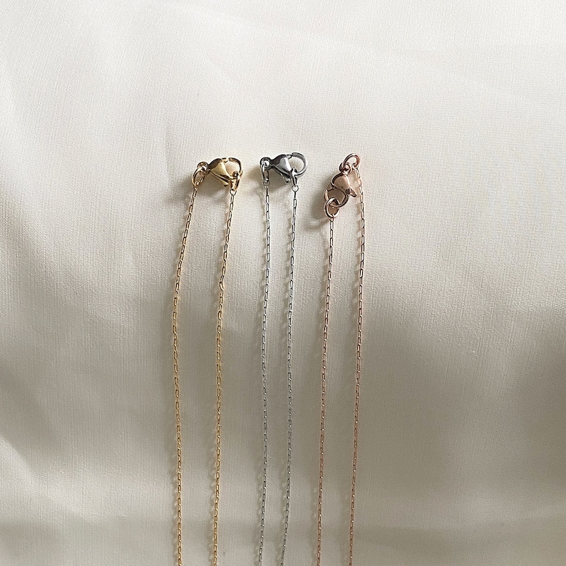 May include: Four different chain necklaces with lobster claw clasps. The chains are gold, silver, and rose gold.