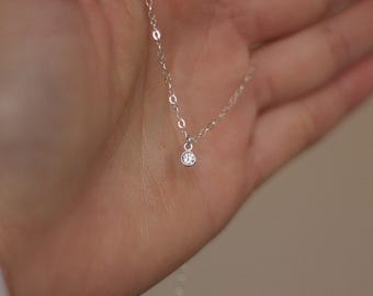 May include: A delicate silver chain necklace with a small, clear gemstone pendant.