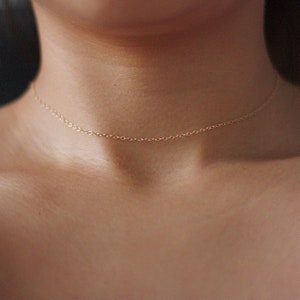 May include: A delicate gold chain necklace worn as a choker.