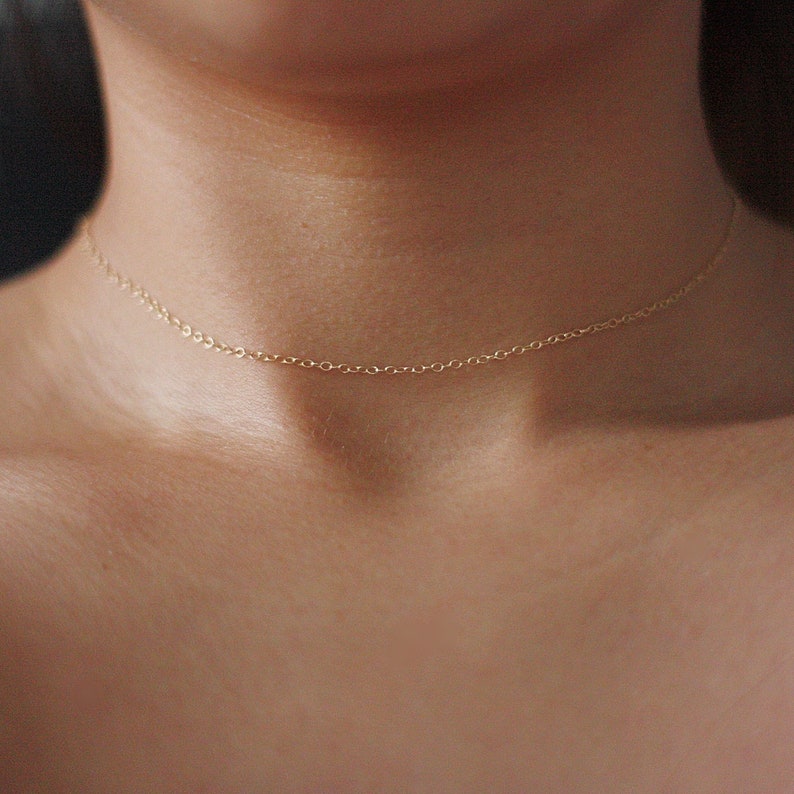 May include: A delicate gold chain necklace worn as a choker.