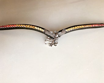 May include: A black leather horse browband with a silver phoenix charm. The browband is decorated with red, orange and yellow rhinestones.