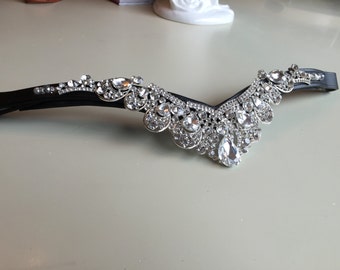 May include: A black leather browband with a large, ornate crystal design. The crystals are clear and faceted, and they are arranged in a cascading pattern.