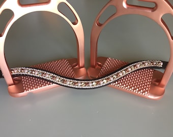May include: A black leather stirrup leather with a row of pink and gold crystals and pearls. The leather is wrapped around two rose gold stirrups.