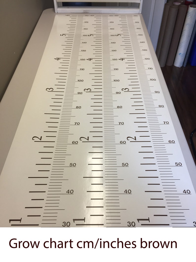 Op de afbeelding: Een witte groeikaart met bruine markeringen in centimeters en inches. De kaart is gemarkeerd van 30 tot 180 centimeter en van 12 tot 72 inch.