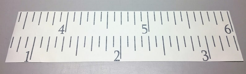 Op de afbeelding: Een witte liniaal met zwarte markeringen, die metingen van 1 tot 6 inch laat zien.
