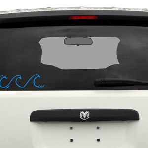 K&ouml;nnte beinhalten: Ein wei&szlig;er SUV mit einem blauen Wellensticker an der Heckscheibe.