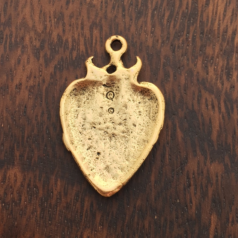 Op de afbeelding: Gouden hartvormige hanger met een getextureerd oppervlak en een lus aan de bovenkant. De achterkant van de hanger heeft twee kleine cirkels.