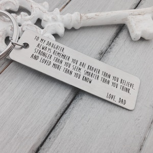 May include: Silver keychain with a message for a daughter from their dad. The message reads: "To my daughter, always remember you are braver than you believe, stronger than you seem, smarter than you think, and loved more than you know. Love, Dad."